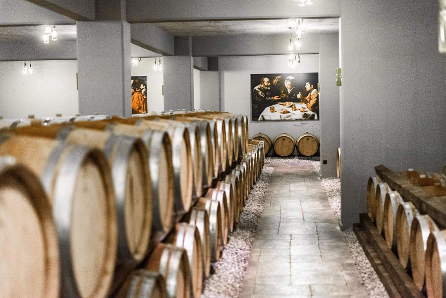 corridor of illuminated 'Oenogenesis Estate' cellar with wine wood barrels on top of each other on the both sides